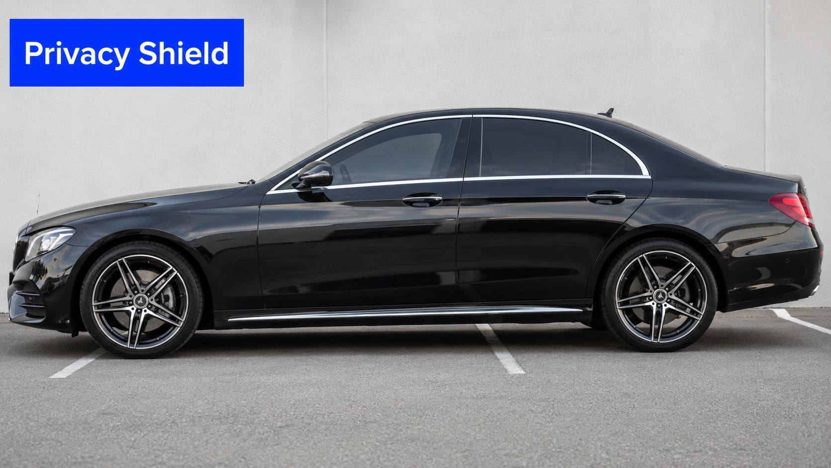 A sleek black luxury sedan with dark tinted windows parked in a paved outdoor lot.