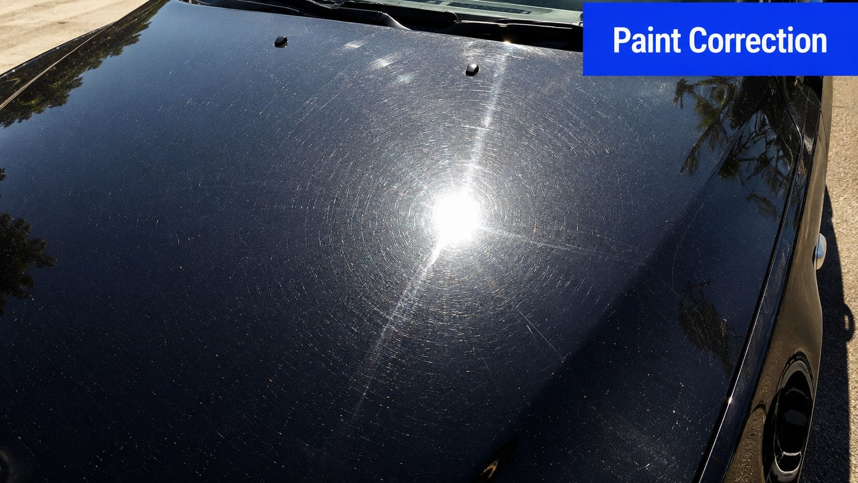 A close-up view of a black car hood showing heavy swirl marks and scratches under sunlight.